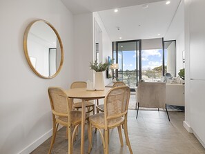 A dining area with a round table, six wicker chairs, a large mirror, and a view of the city through large windows. - Bright 1-bedroom Escape With Private BBQ (Perth)