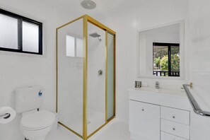 A bathroom with a white toilet, a glass-enclosed shower, a white sink, and a window with a view of greenery. - Homely 3-bed Townhouse With Pool & Gym Access (Brisbane)