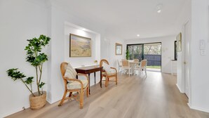 A dining area with a wooden table and wicker chairs, a potted plant, and a painting on the wall. - Homely 3-bed Townhouse With Pool & Gym Access (Brisbane)