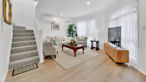 A living room with a staircase, a sofa, a coffee table, a TV, and a plant. - Homely 3-bed Townhouse With Pool & Gym Access (Brisbane)