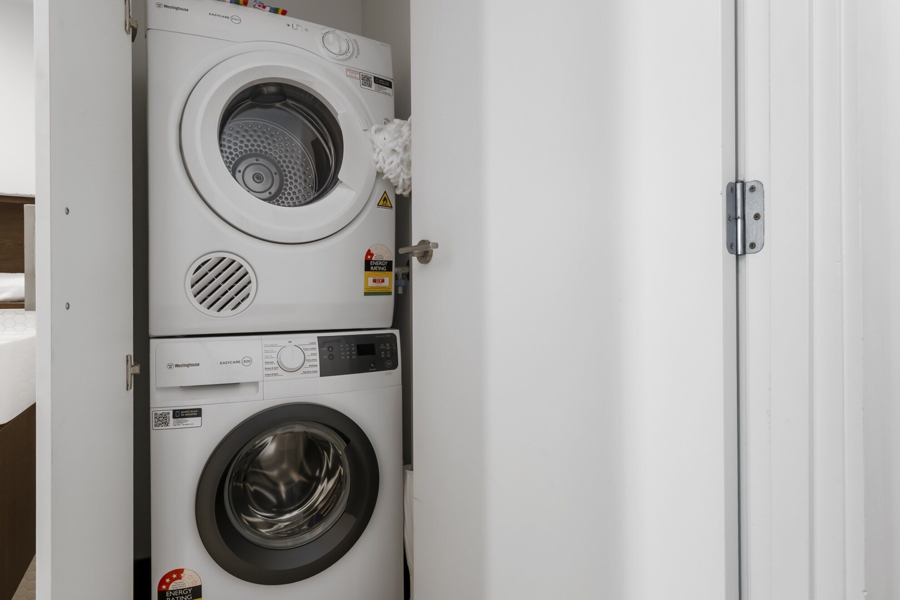 A stacked washer and dryer unit with a control panel and safety labels.