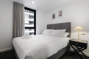 A hotel room with a large bed, a bedside table with a lamp, and a window with curtains.
