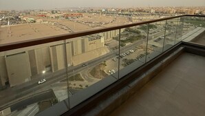 A balcony with a glass railing overlooking a cityscape with buildings and roads.