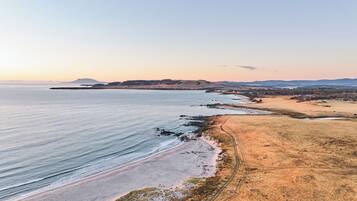 Un paysage côtier avec une plage, un sentier de terre et des collines à l’horizon.