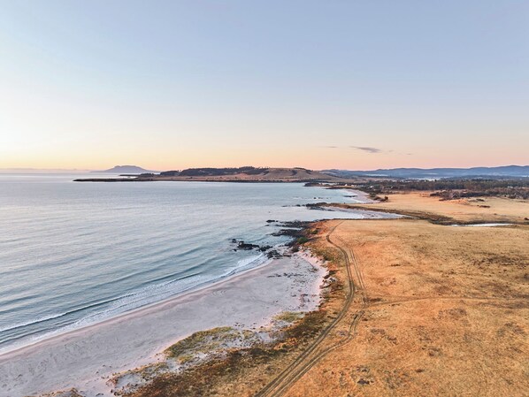 Eine Küstenlandschaft mit Strand, Feldweg und Hügeln in der Ferne.