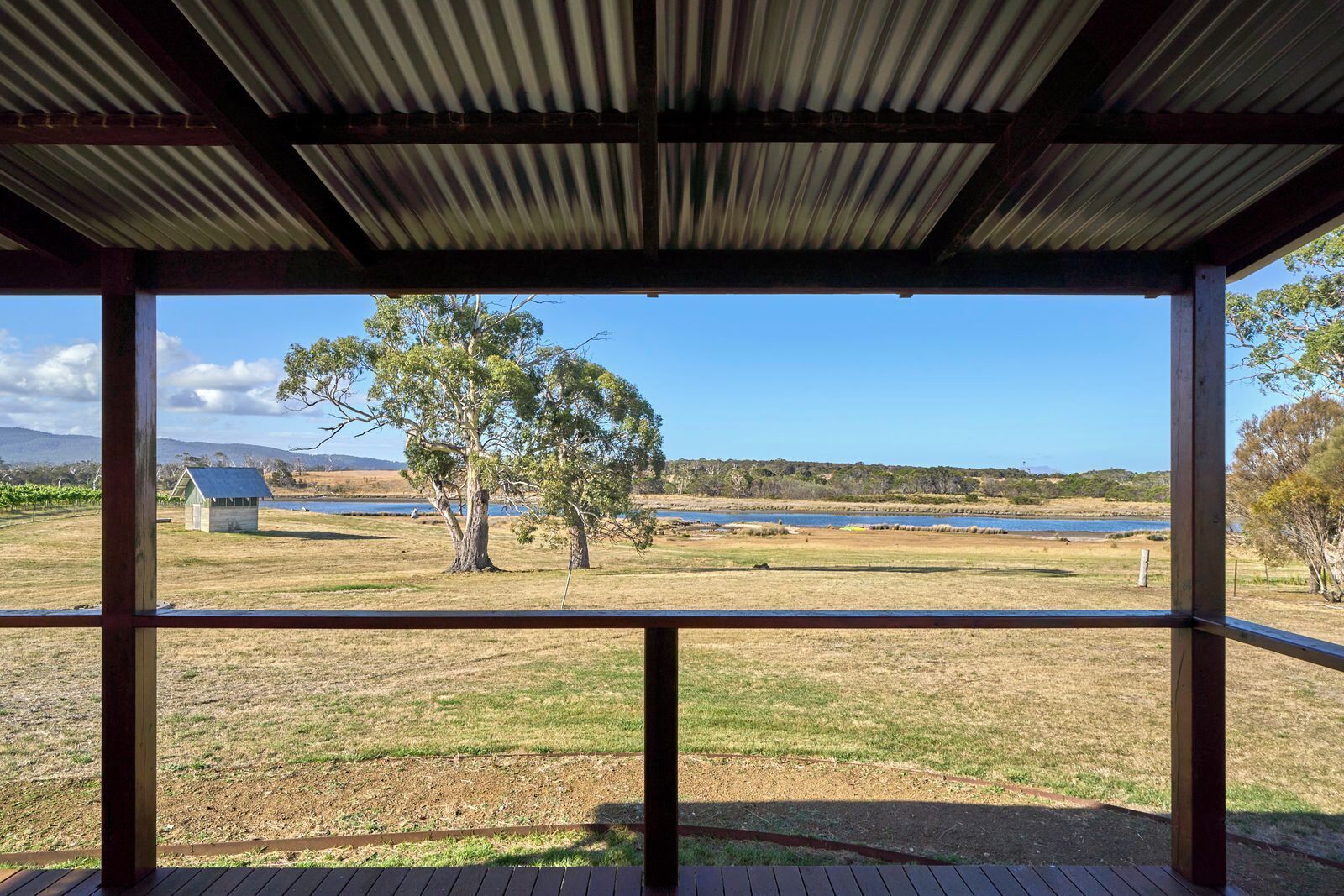 A covered outdoor area with a view of a lake, trees, and a distant building.