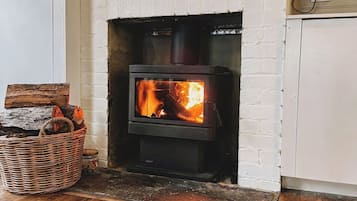A wood-burning stove in a room with a white brick wall, a wooden floor, and a basket of firewood.