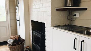 Een keuken met een witte bakstenen muur, een zwart fornuis, een houten vloer en een metalen waterkoker op een plank.