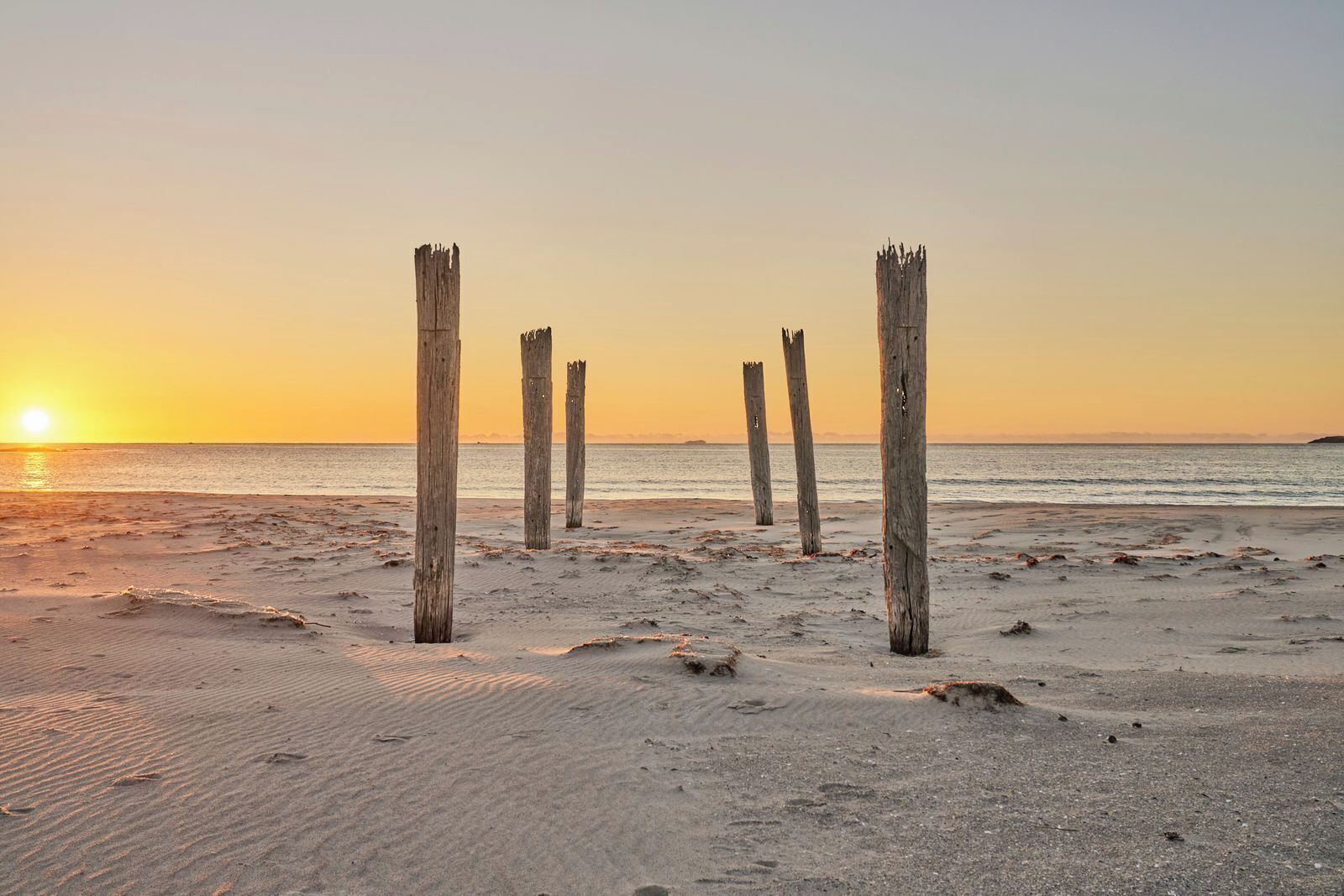 A beach with wooden posts and a sunset.