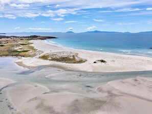A beach with clear water, distant mountains, and a clear sky.