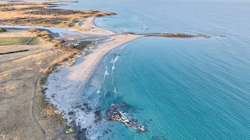 Una vista aerea di una zona costiera con spiaggia, costa rocciosa e campi coltivati.