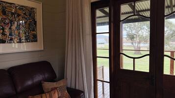 A room with a leather sofa, a framed abstract painting, and a view of a grassy area through a wooden door with glass panels.