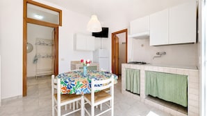 Uma cozinha com mesa de jantar, cadeiras, luminária pendente, fogão e televisão.