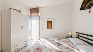 Quarto com cama, guarda-roupa, mesa de cabeceira e janela com cortinas.