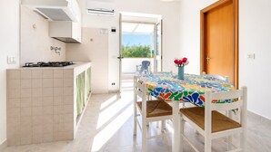 Uma cozinha com fogão, uma mesa de jantar com toalha de mesa colorida e vista através de uma porta aberta.