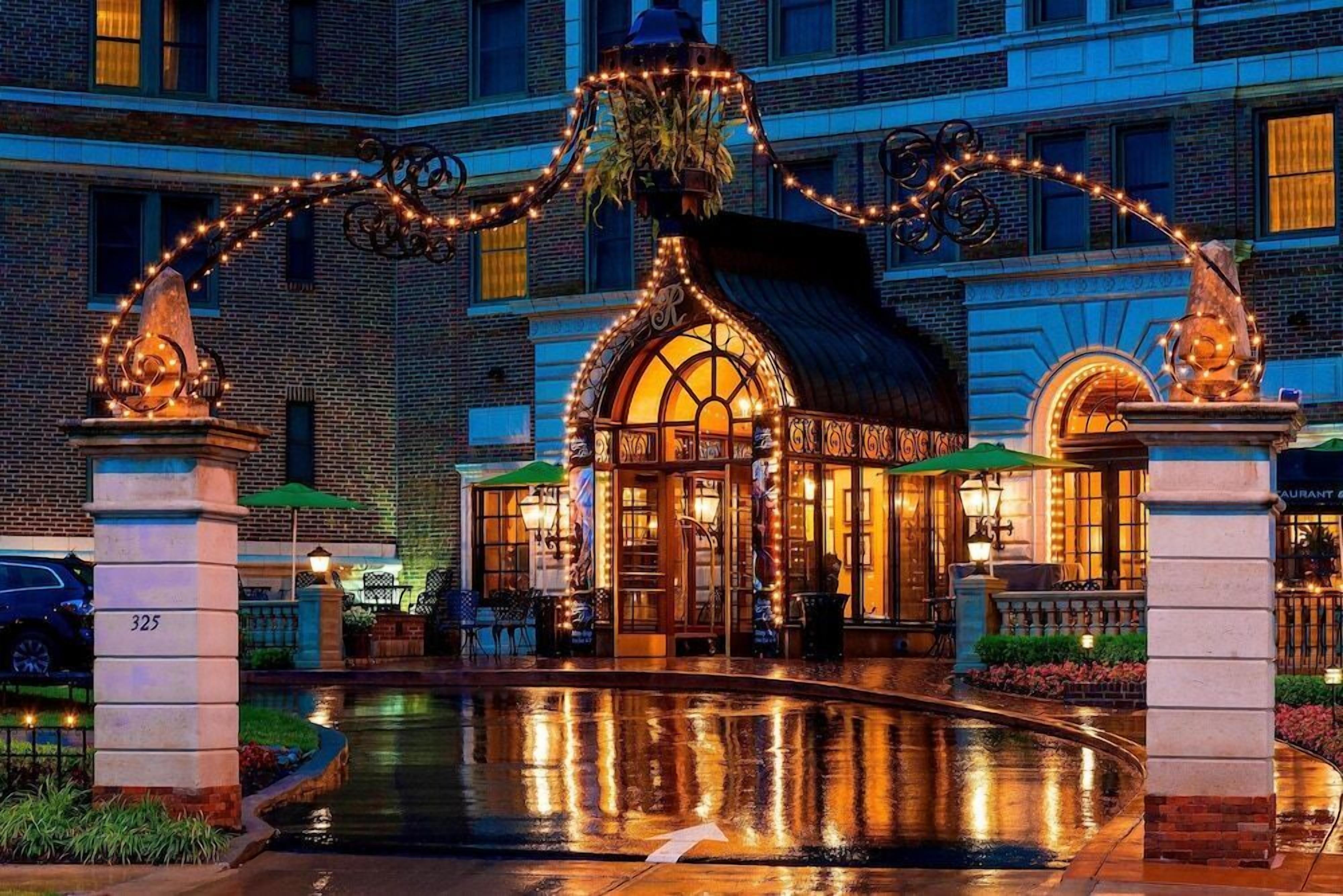A hotel entrance with a fountain, ornate metalwork, and a warm-lit building facade.