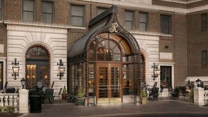 A hotel entrance with a glass facade, a prominent 'R' logo, and outdoor seating.