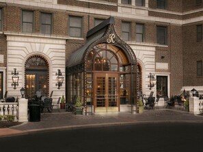 L’entrée d’un hôtel se distingue par sa façade en verre, un logo « R » bien visible et des places assises à l’extérieur.