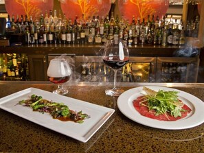 A bar setting with a variety of bottles, two glasses of wine, and a plate of food. - 1-Bedroom Suite at a 4⭐️ Hotel (Kansas City)