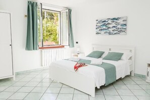 A bedroom with a bed, a window with curtains, a bedside table, and a wall-mounted artwork. - Villa Acquamarina (Sorrento)
