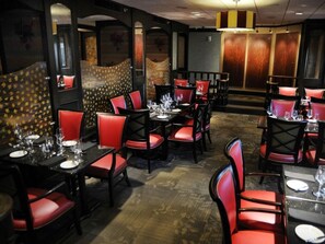 Ein Restaurant mit roten Sitzmöbeln, schwarzen Tischen, einer Wand mit Muster und einer Holztür.