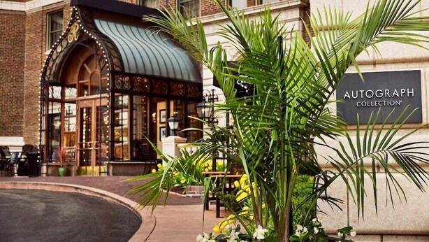 A building with a sign for an autograph collection and a covered entrance with decorative lights.