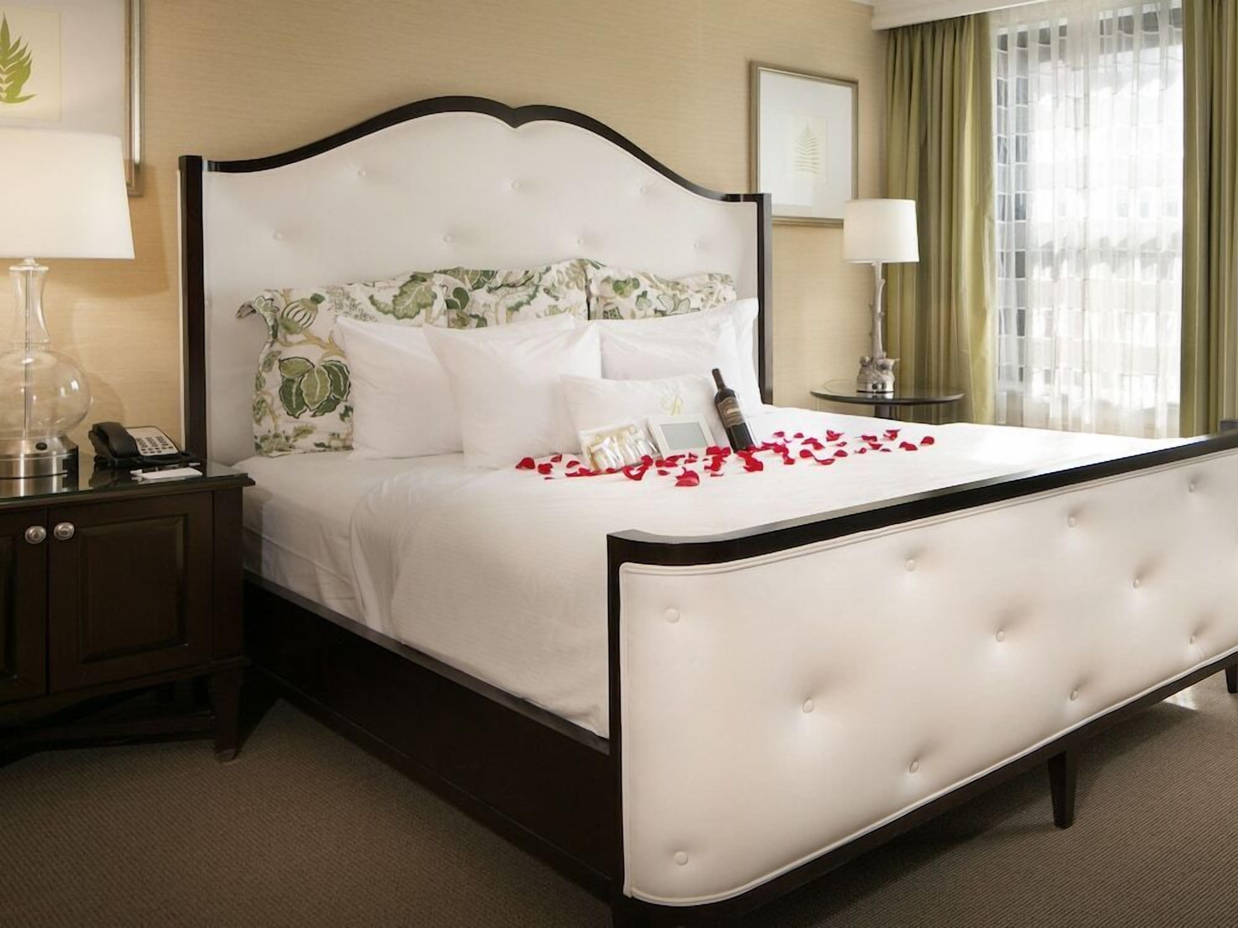 A hotel room with a large bed, a bedside table with a lamp, and a window with curtains.