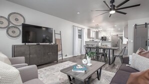 Una sala moderna con un televisor de pantalla plana, un sofá, una mesa de centro y un comedor con una cocina al fondo.