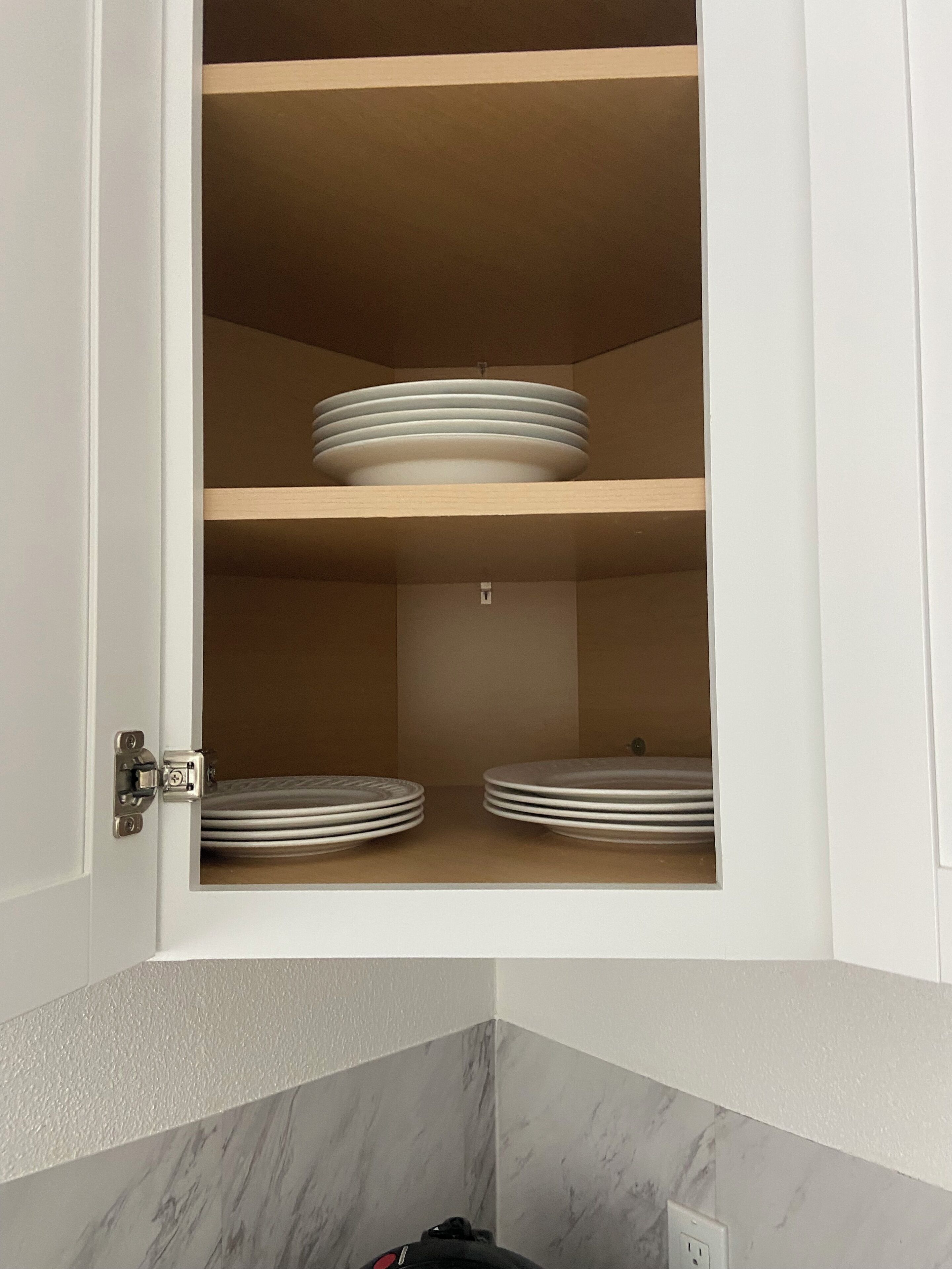 A white cabinet with a marble countertop below, containing two shelves with stacked plates.
