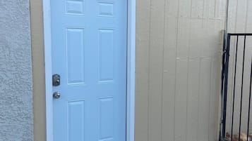A light blue door with a keypad lock, set in a beige wall with a metal gate to the right.