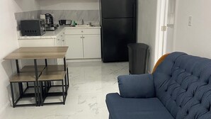 Una cocina moderna con armarios blancos, un refrigerador negro, una mesa de comedor con sillas y un sofá azul.