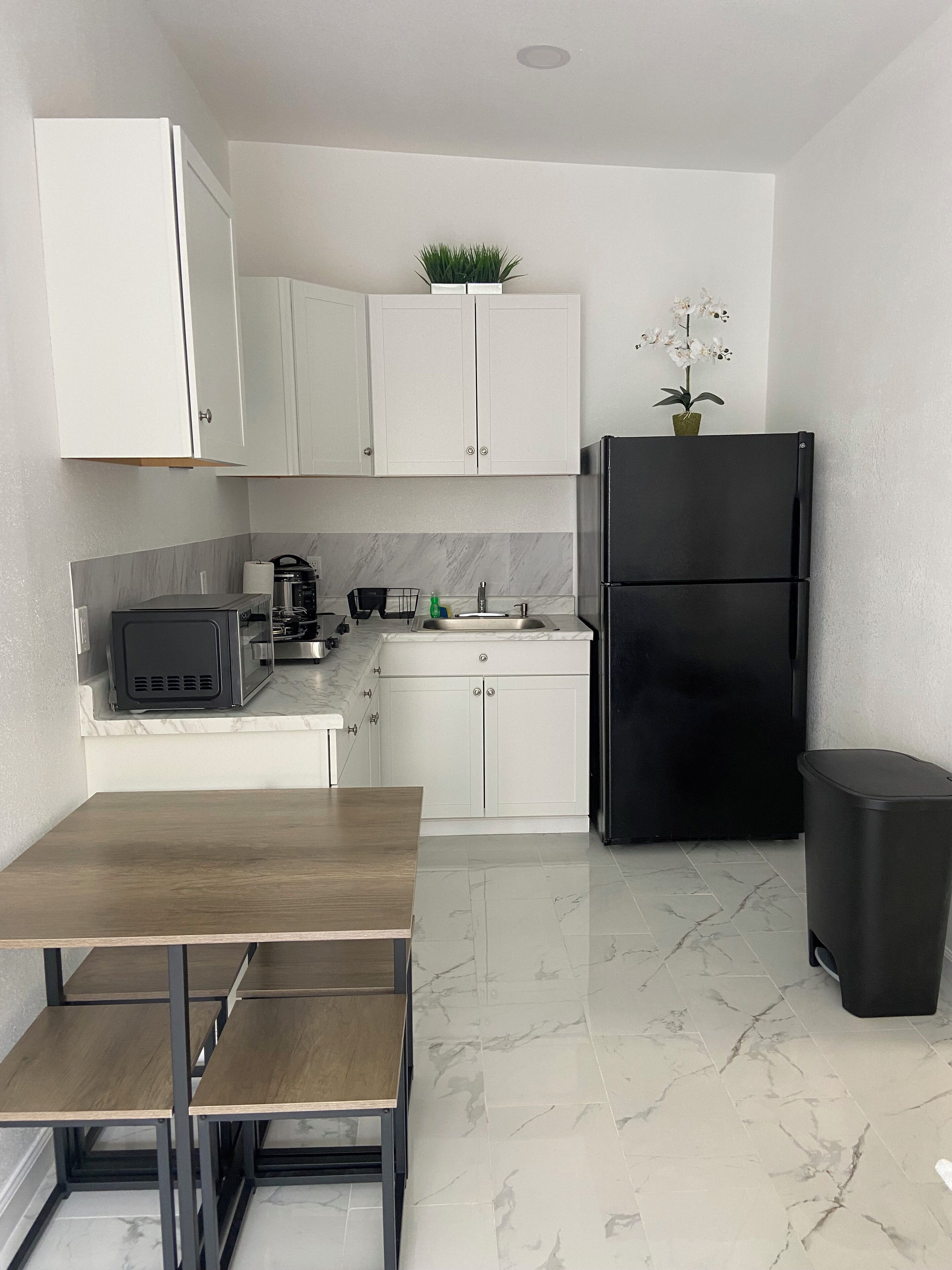 Una cocina moderna con armarios blancos, un refrigerador negro, una mesa de madera y un piso de mármol.