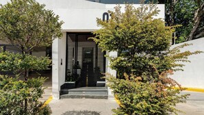 A modern building entrance with a black gate, surrounded by greenery and a concrete pathway.