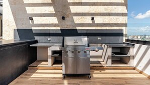 A rooftop barbecue area with a stainless steel grill, two side burners, and a built-in oven.
