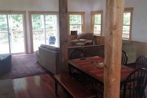 A room with a wooden dining table, chairs, a sofa, and a large window. - Enchanting pet-friendly and private cabin with cozy pellet fireplace (Putney)