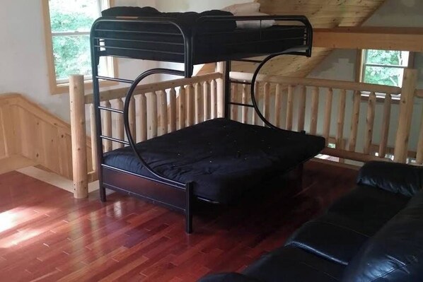 A bunk bed with a mattress, a wooden railing, and a black leather sofa. - Enchanting pet-friendly and private cabin with cozy pellet fireplace (Putney)