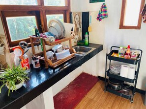 A kitchen with a black countertop, a wooden drying rack, a sink, and a black metal rack with food items.