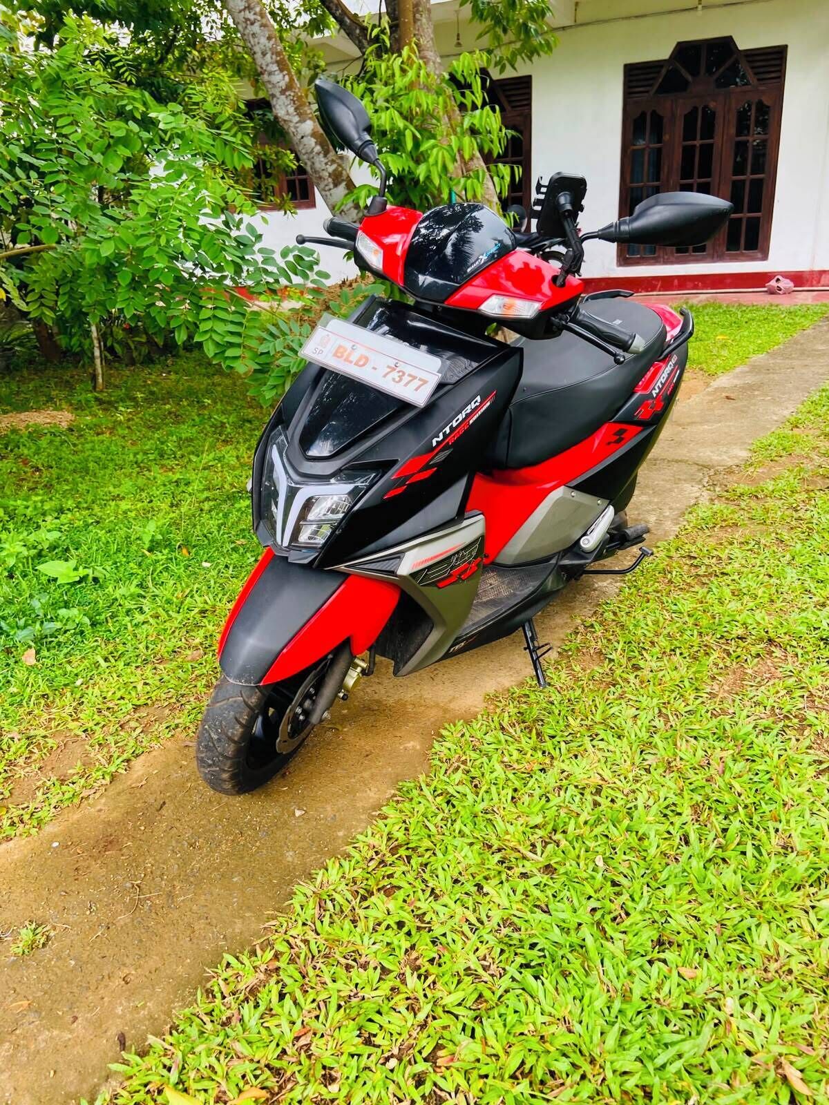Ein rotes und schwarzes Motorrad steht auf einem unbefestigten Weg, der von Gras gesäumt ist.