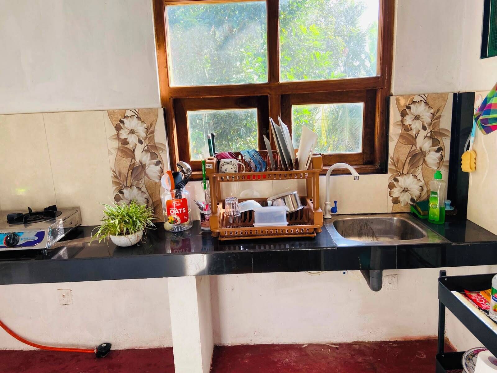 A kitchen with a gas stove, a sink, a window with a view of greenery, and a dish rack with utensils.