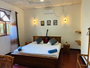 Ein Schlafzimmer mit einem Bett, einer Gitarre, einem Nachttisch, einem Sessel und einem Fenster mit Vorhängen.