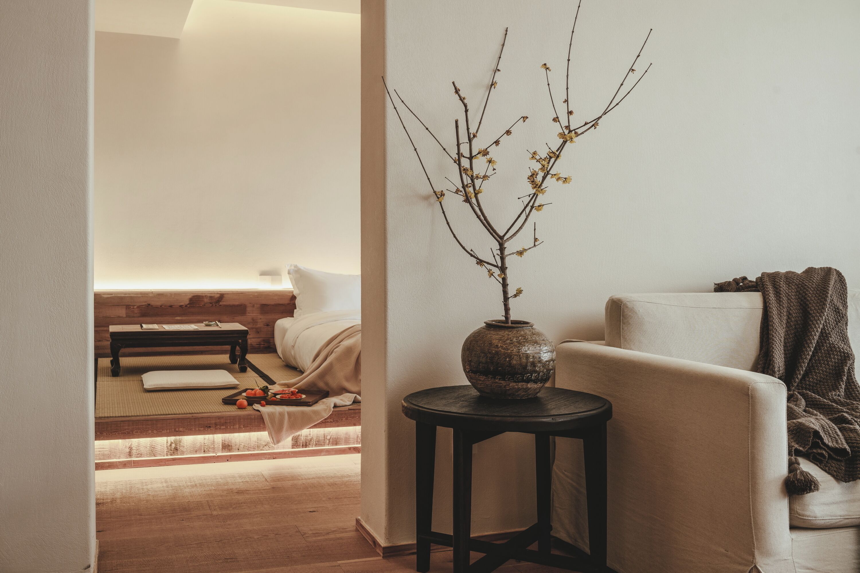 Una habitación minimalista con una cama, una mesita con un jarrón y un sofá.