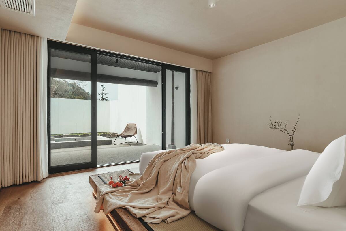 A modern hotel room with a large bed, a sliding glass door leading to a balcony, and a view of the outdoors.