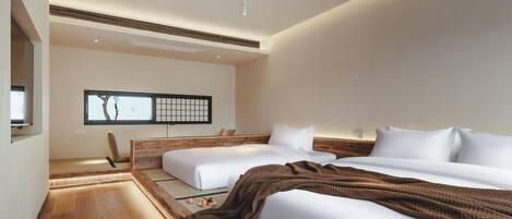 Quarto de hotel moderno com duas camas, piso de madeira, esteira de tatame, janela ampla com vista e televisão fixada na parede.