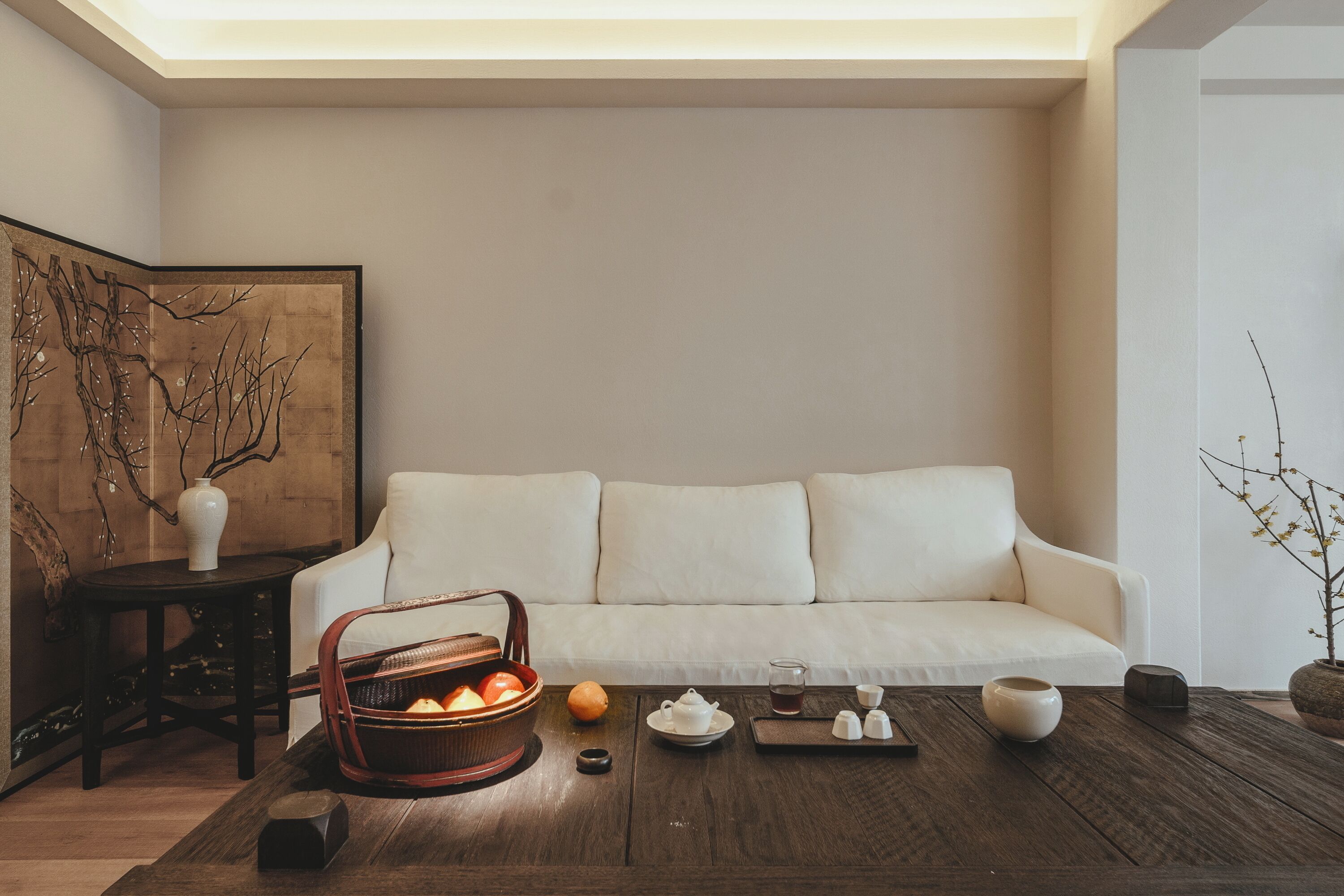 Ein modernes Wohnzimmer mit einem weißen Sofa, einem Holztisch mit Tee-Set und einer dekorativen Vase.