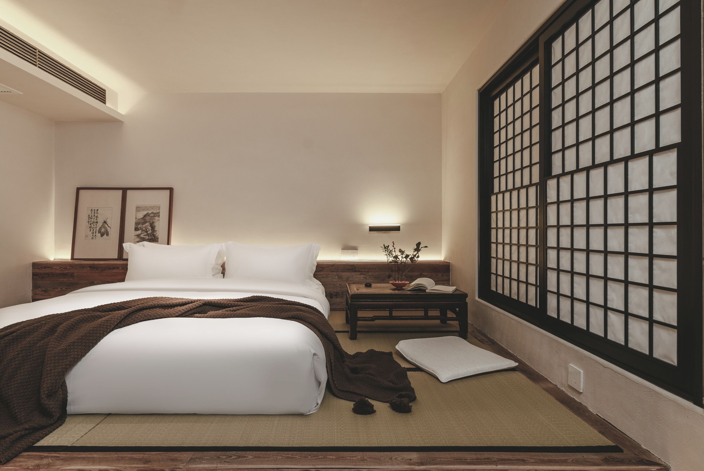 A hotel room with a bed, bedside table, and a view of a traditional Japanese screen.