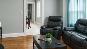 A modern living room with a dark leather sofa, a wooden coffee table with a plant, and a ceiling light fixture. - Heated Winter Stay • 3BR Home • Pet-Friendly • Free Parking • Near Hospitals • 6 (Manchester)