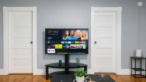 A living room with a flat-screen TV mounted on the wall, a dark wooden coffee table with a potted plant, a remote control, and decorative items. - Heated Winter Stay • 3BR Home • Pet-Friendly • Free Parking • Near Hospitals • 6 (Manchester)