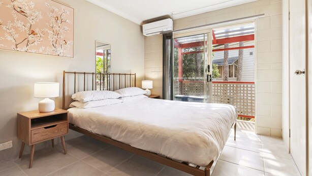 A bedroom with a bed, bedside tables, a wall-mounted air conditioner, and a sliding glass door leading to an outdoor area. - Comfy Studio Near Gabba With Secure Parking (Brisbane)