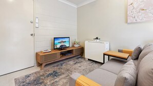 A modern living room with a TV, wooden furniture, a white refrigerator, and a beige sofa. - Comfy Studio Near Gabba With Secure Parking (Brisbane)