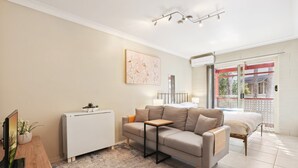 A modern living room with a sofa, a small table, a TV, and a radiator. - Comfy Studio Near Gabba With Secure Parking (Brisbane)